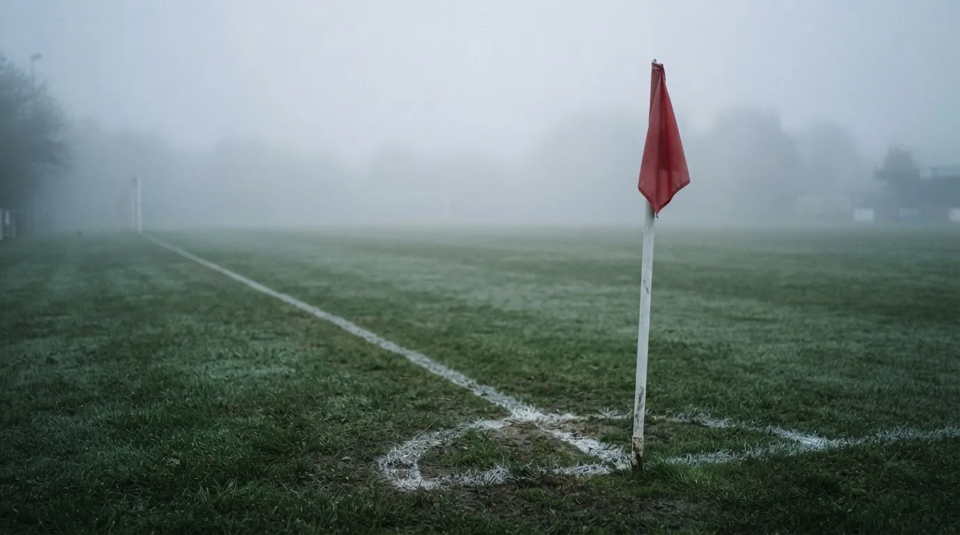 Der Rand eines Spielfelds mit weißer Linie und Eckfahne bei Nebel am frühen Morgen, ohne Menschen.