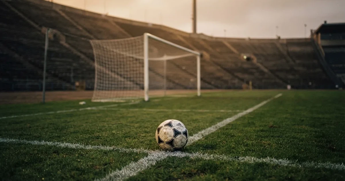 Ein Fußball liegt im Strafraum direkt vor dem Tor mit Netz, im Hintergrund leere Ränge bei Dämmerung.