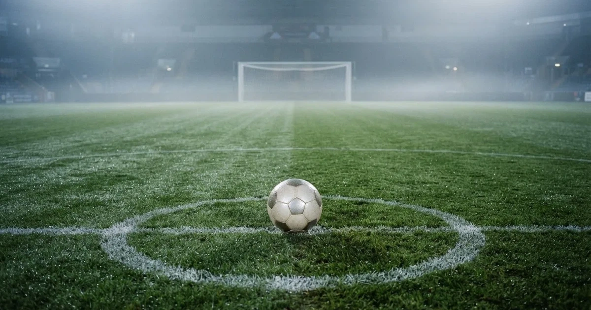 Ein Fußballtor mit gespanntem Netz steht auf einem leeren Rasenplatz, davor ein einzelner Ball, Morgendunst liegt über dem Feld.