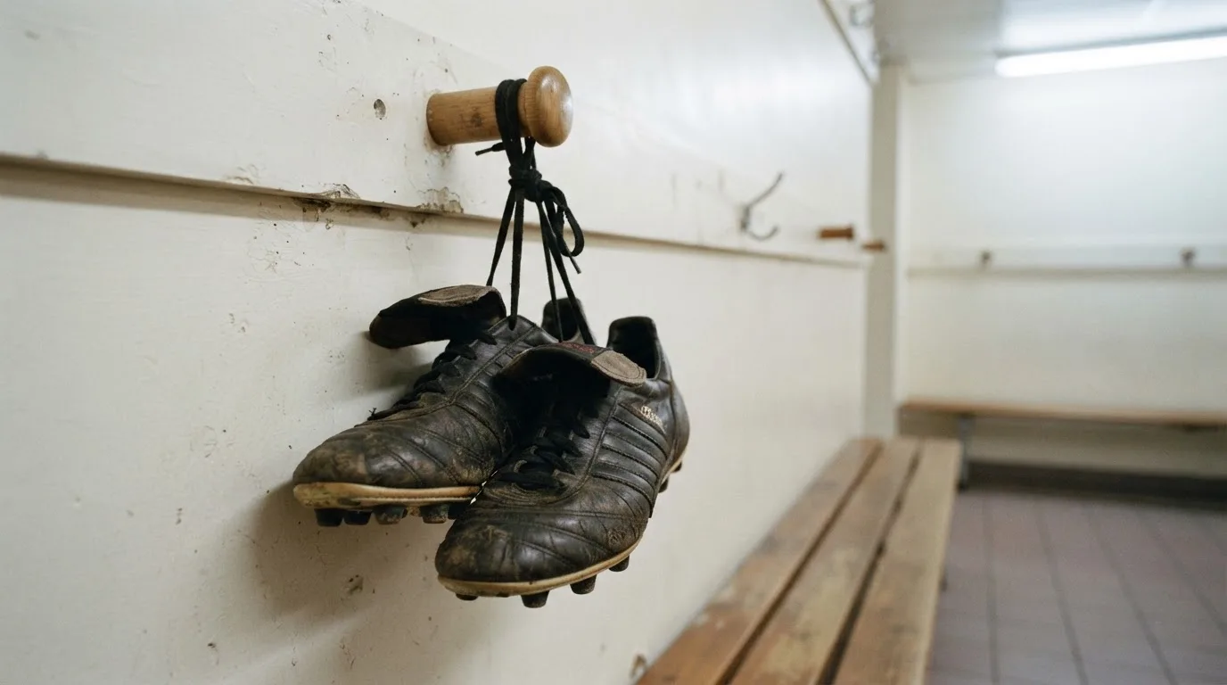 Ein Paar Fußballschuhe hängt an den Schnürsenkeln an einem Holzhaken in einer leeren Umkleidekabine.