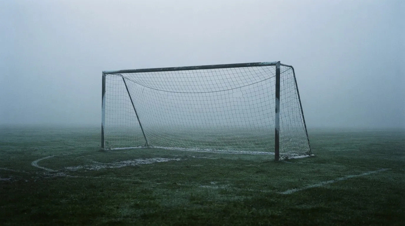 Ein Fußballtor mit Netz im Morgennebel auf einem leeren Platz, die Linien nur schwach zu erkennen.