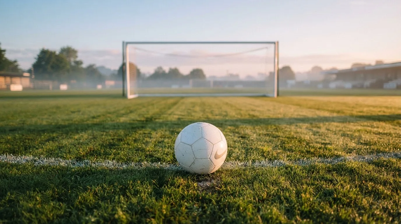 Ein Fußball auf dem Rasen vor einem leeren Tor im frühen Morgenlicht.