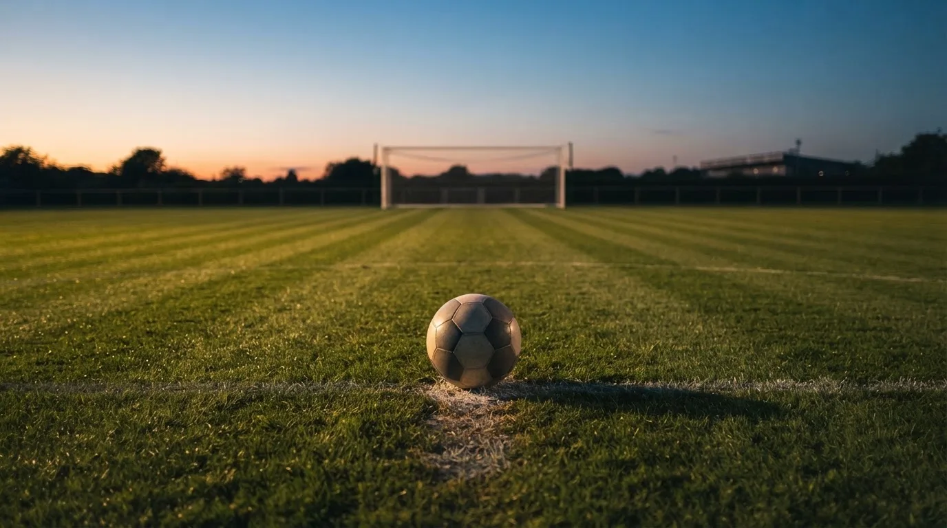 Ein Fußball liegt auf dem Elfmeterpunkt eines leeren Platzes im Abendlicht.