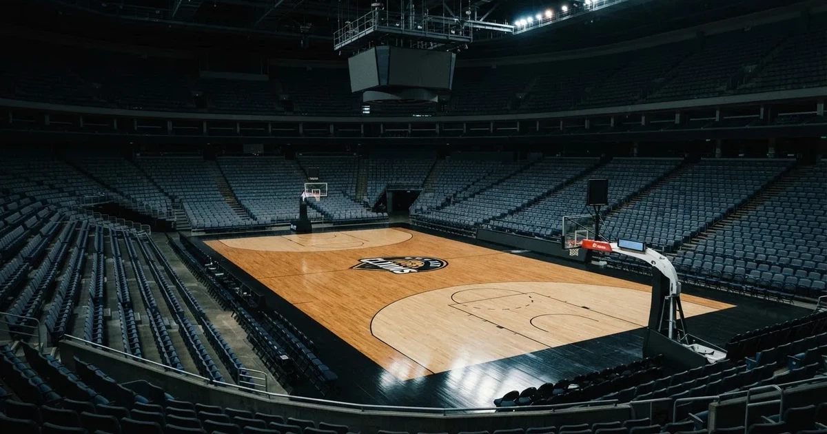 Eine leere Basketballhalle von einer oberen Tribünenreihe aus gesehen, Parkett und Körbe im Licht der Hallenstrahler.