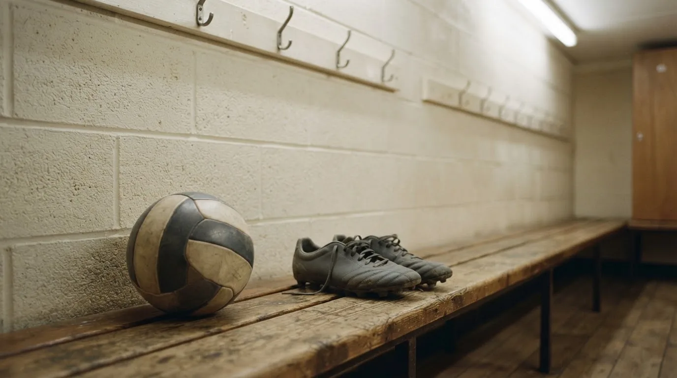 Ein Fußball liegt auf einer Holzbank in einer leeren Umkleide neben einem Paar Fußballschuhen ohne Markenzeichen.