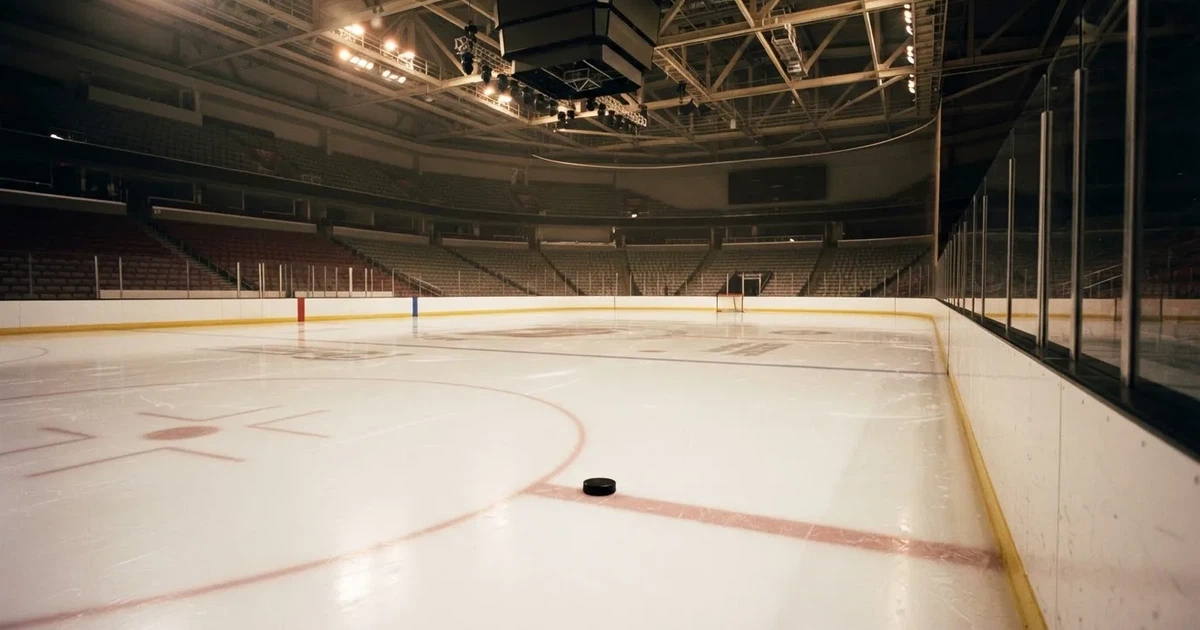 Eine leere Eisfläche in einer Halle mit Banden und Flutlicht, auf dem Eis liegt ein einzelner Puck.
