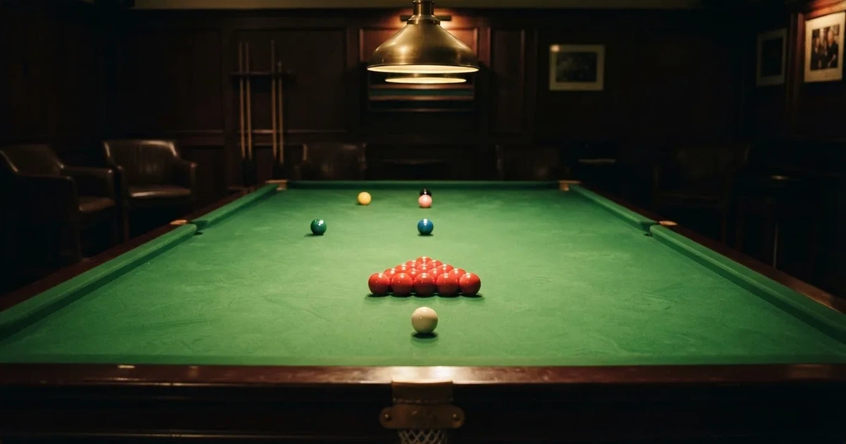 Ein Snookertisch mit grünem Tuch und aufgebauten roten Kugeln in einem abgedunkelten Raum unter einer hängenden Lampe.
