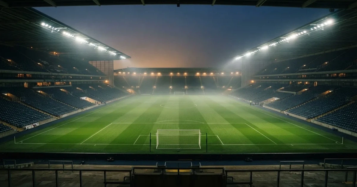 Ein leeres Stadion unter Flutlicht aus großer Entfernung gesehen, Dunst liegt über dem Rasen, die Tribünen sind nur als Lichtpunkte erkennbar.